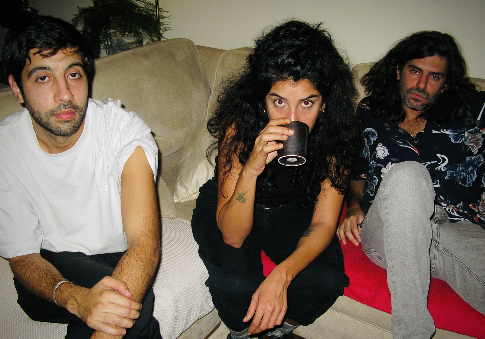 A photo of the three members who are sitting on a couch. In the middle is Sandy Chamoun, sipping from a cup.